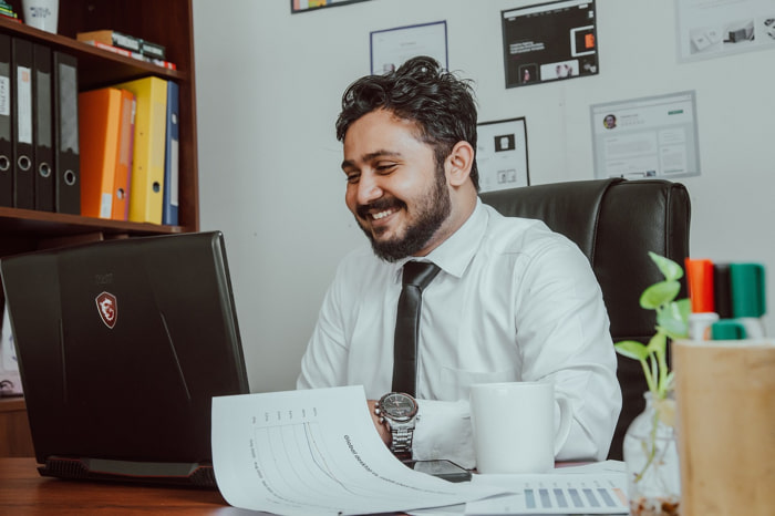 Un manager HR soddisfatto con barba e camicia bianca e cravatta scura nel suo ufficio | Qipo