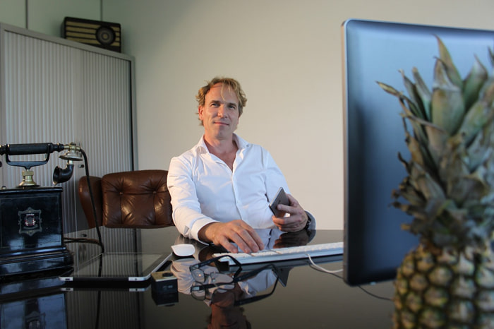 Un responsabile delle risorse umane biondo con camicia bianca nel suo ufficio lavora con il suo laptop | Qipo